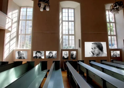 Auf dem Foto ist zu sehen, wie die schwarz-weiß Portraits unterschiedlicher Menschen an der linken Wand in der Stadtkirche Offenbach gezeigt werden.